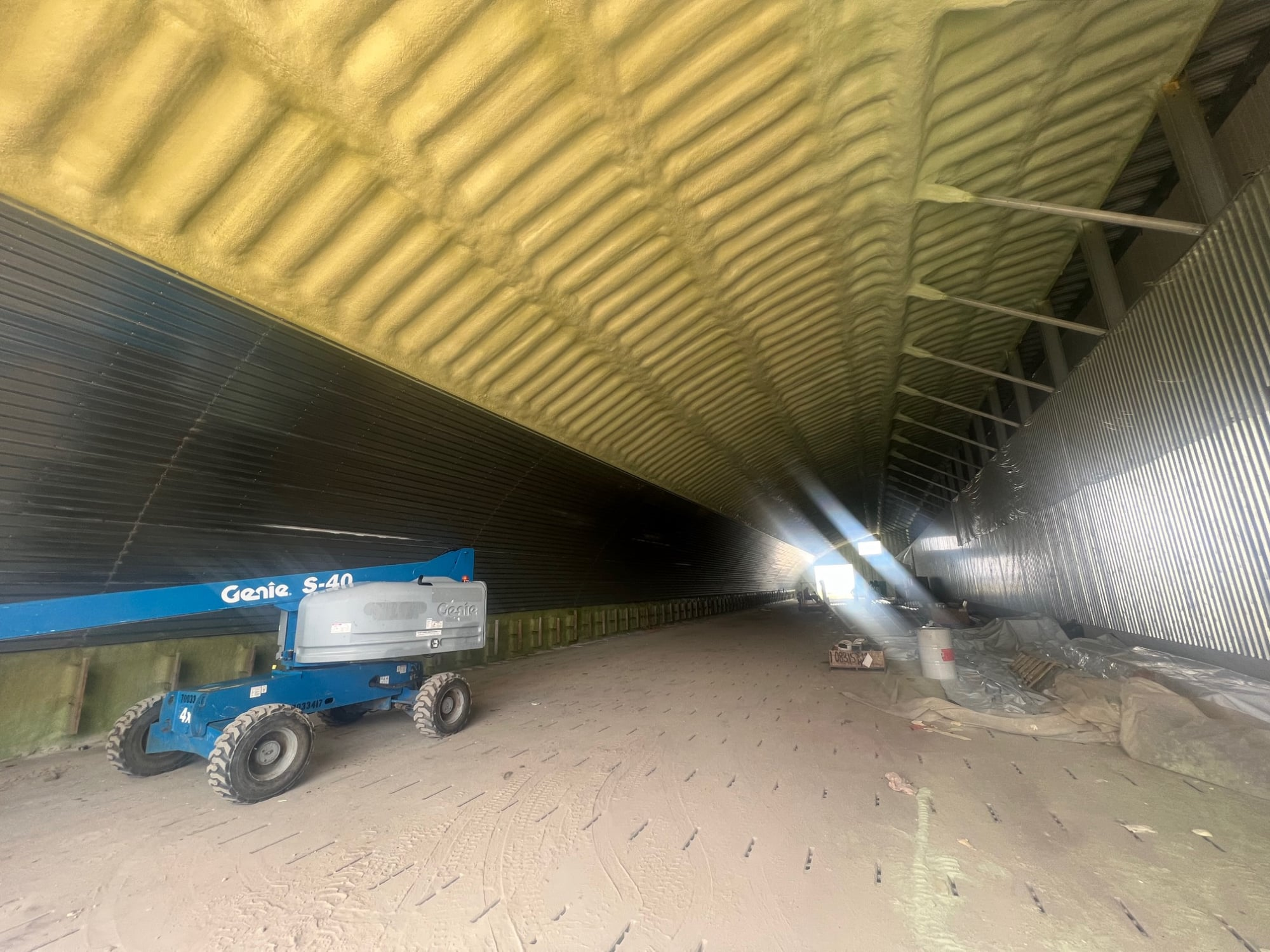 High view down a large farm building with closed-cell foam on the arched ceiling and a boom lift on the floor.