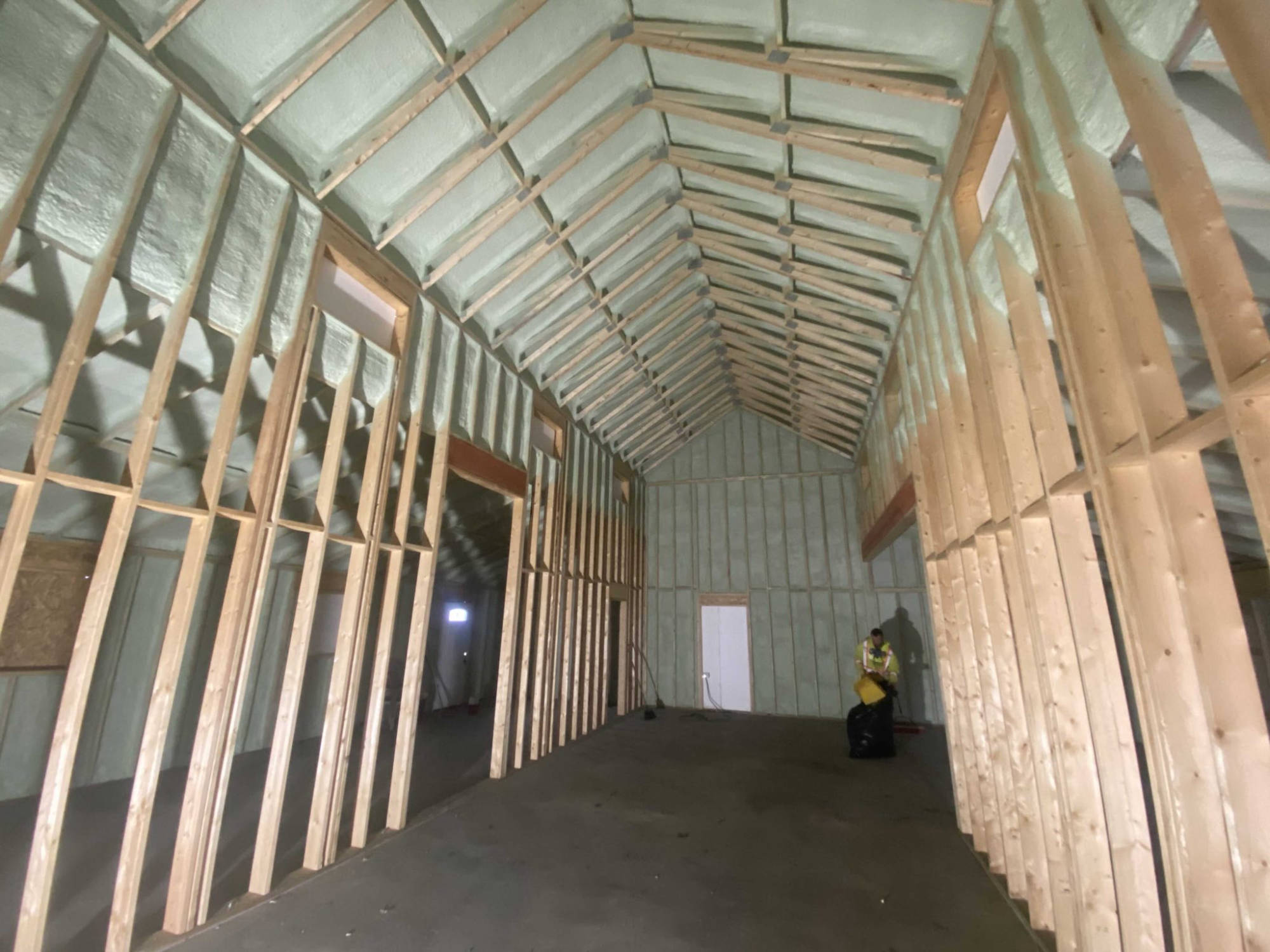 Long framed building with closed-cell foam in the walls and rafters, a worker in a high-vis vest at the far end.