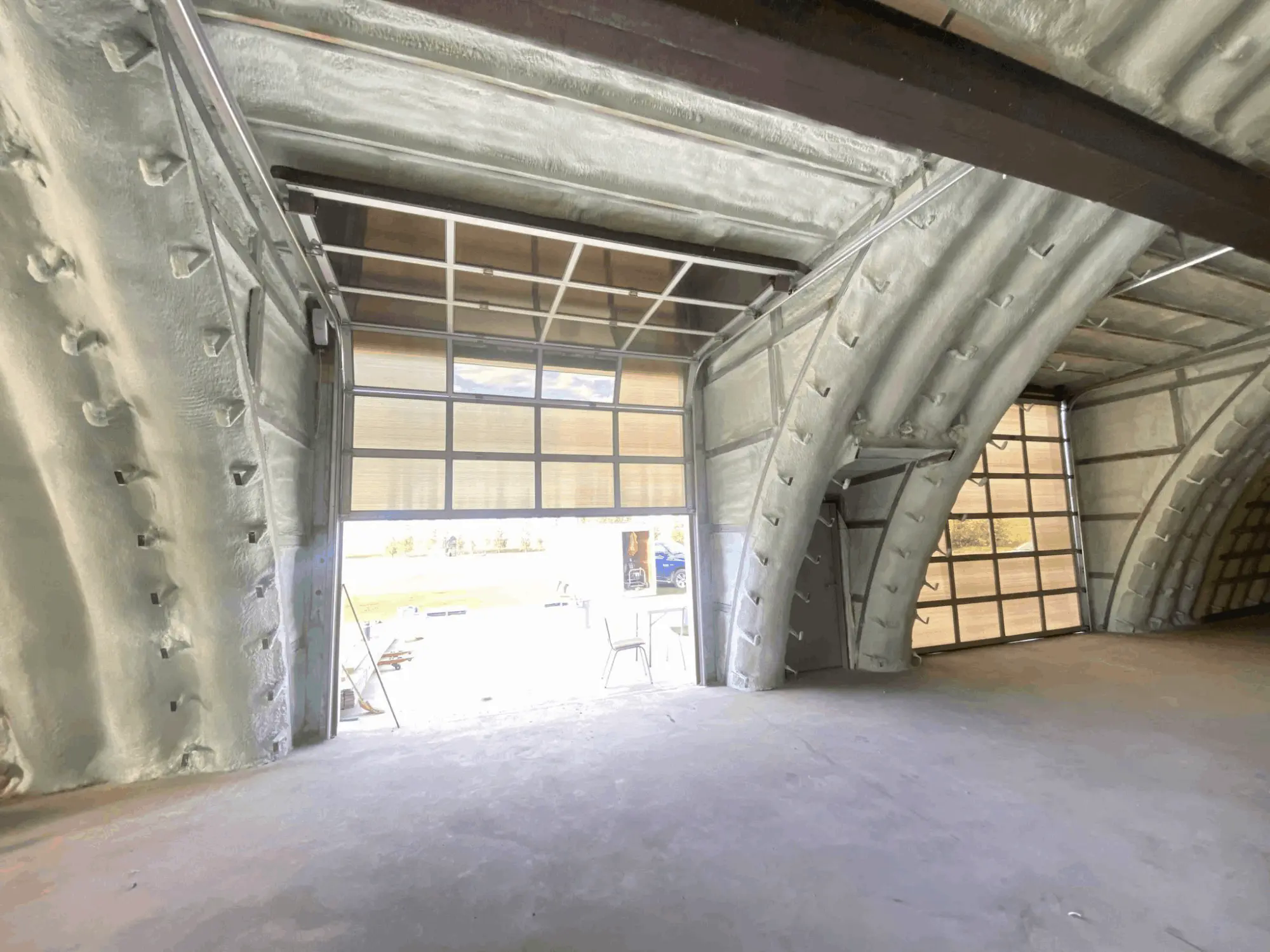Closed-cell spray foam covering the interior of a large arched Manitoba building, looking toward open bay doors.