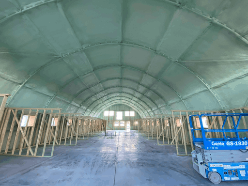 Arched metal building interior with closed-cell foam on the shell and wood-framed bays along a concrete aisle.