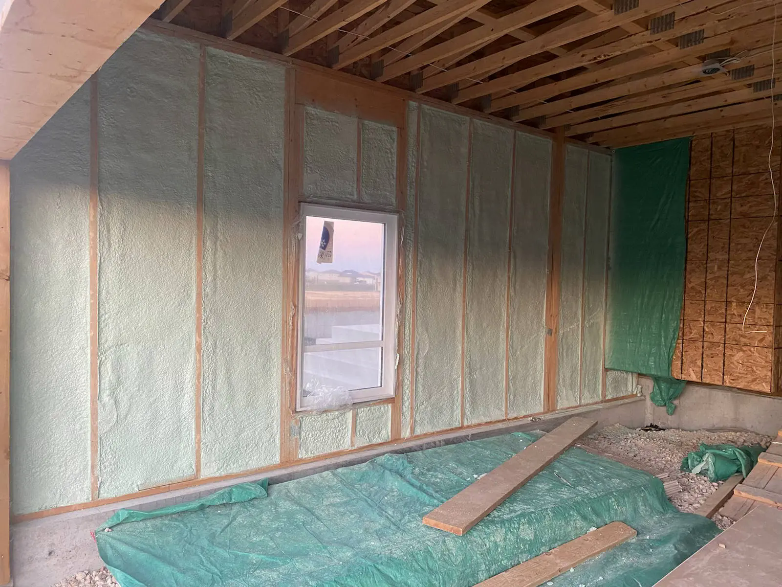 Closed-cell spray foam filling stud cavities on a house wall, with a window and open framing.