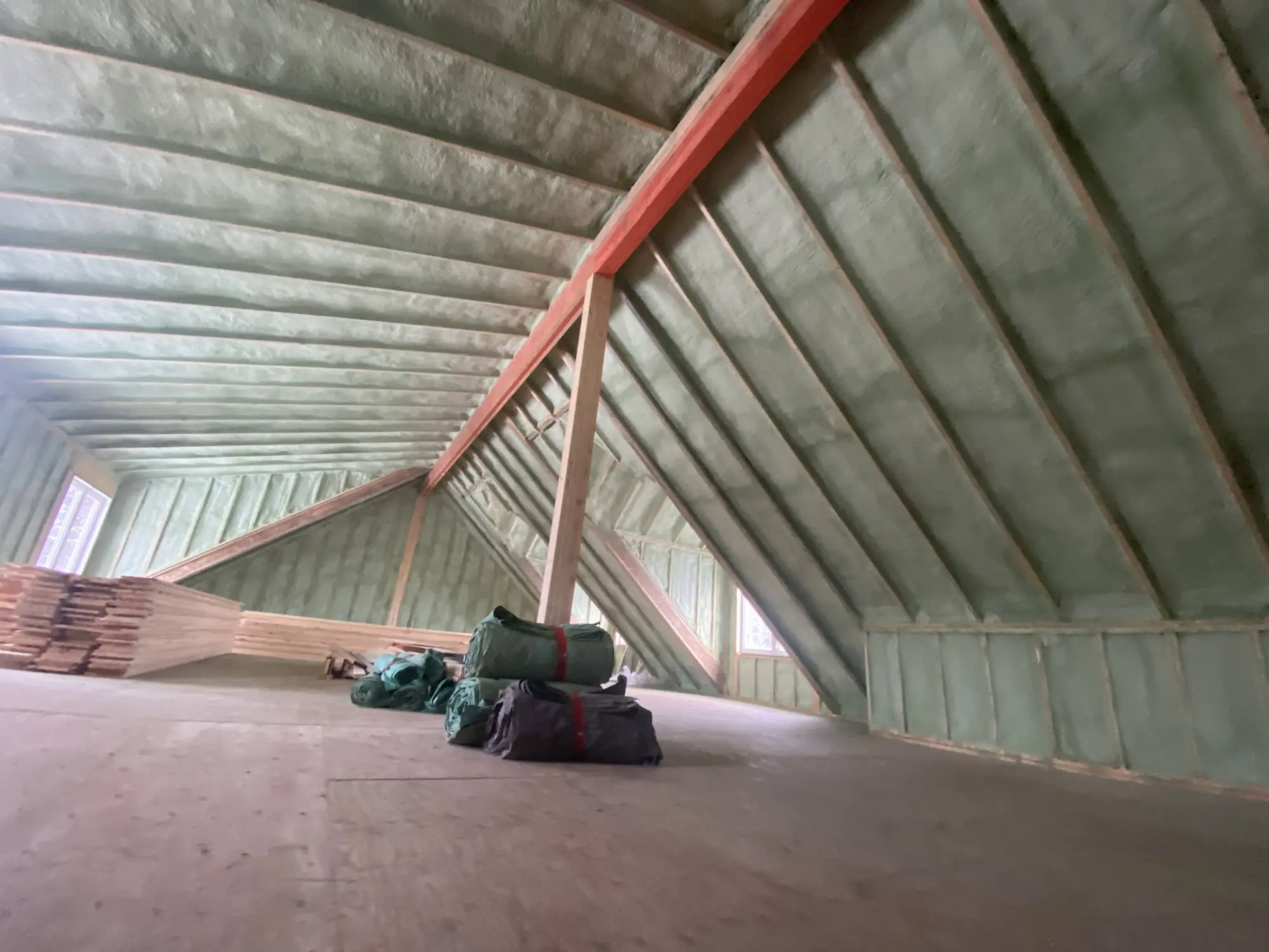 Closed-cell spray foam applied between rafters in a large unfinished attic.