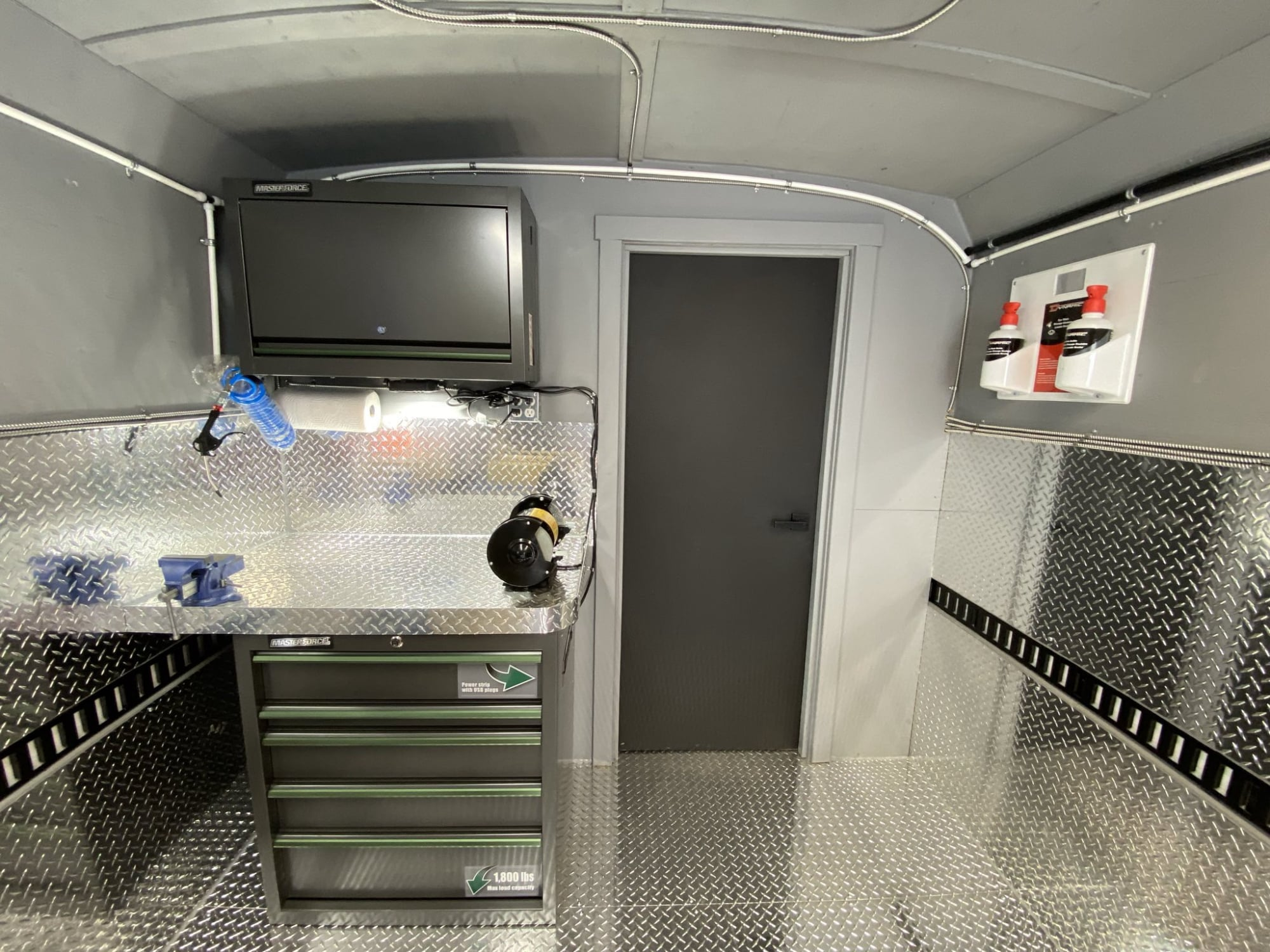 Interior of a custom spray foam rig: diamond-plate workbench, tool chest, monitor and E-track on the walls.