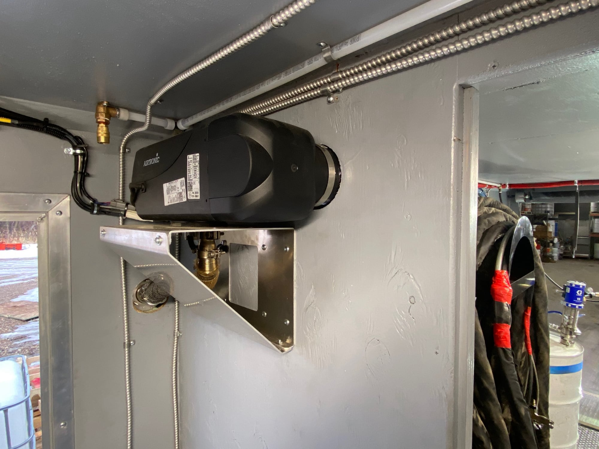 Eberspacher diesel air heater mounted on a custom bracket, with conduit and a chemical drum beyond.