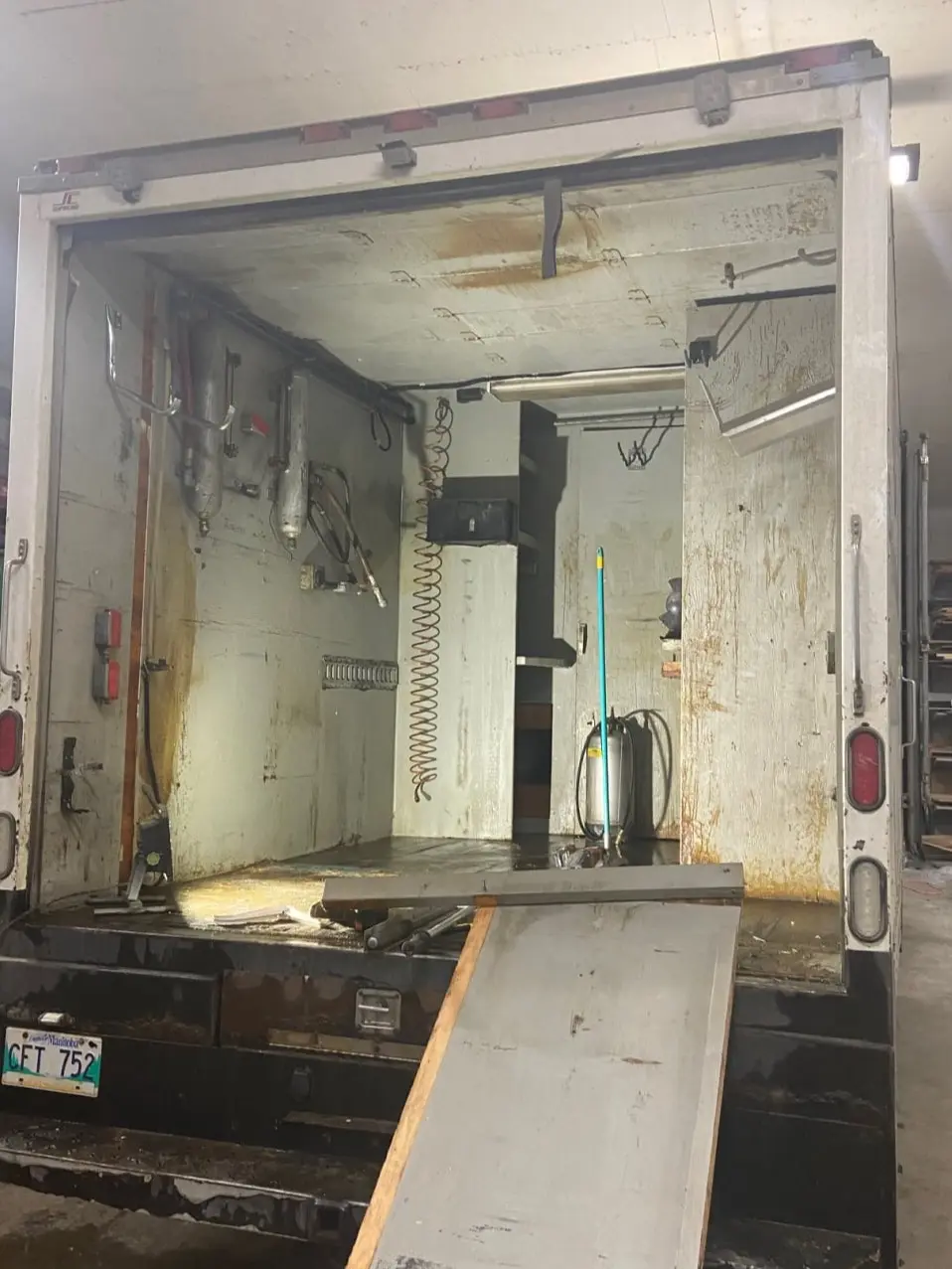Open rear of a spray foam truck with tanks, hoses and a Manitoba plate, ramp on the ground.